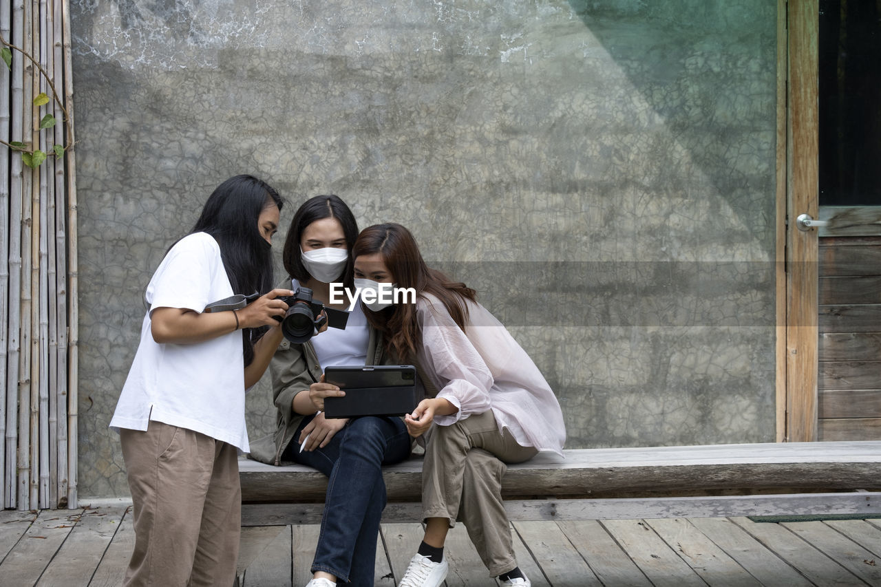 Three women look at their photos against the backdrop outside a cafe building.