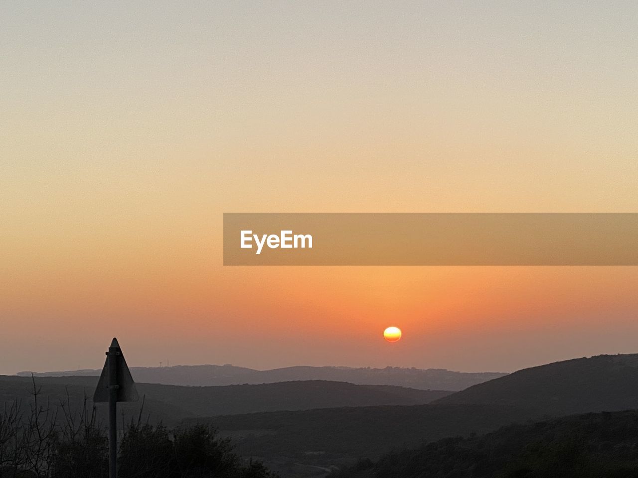 SILHOUETTE MAN STANDING ON MOUNTAIN AGAINST ORANGE SKY