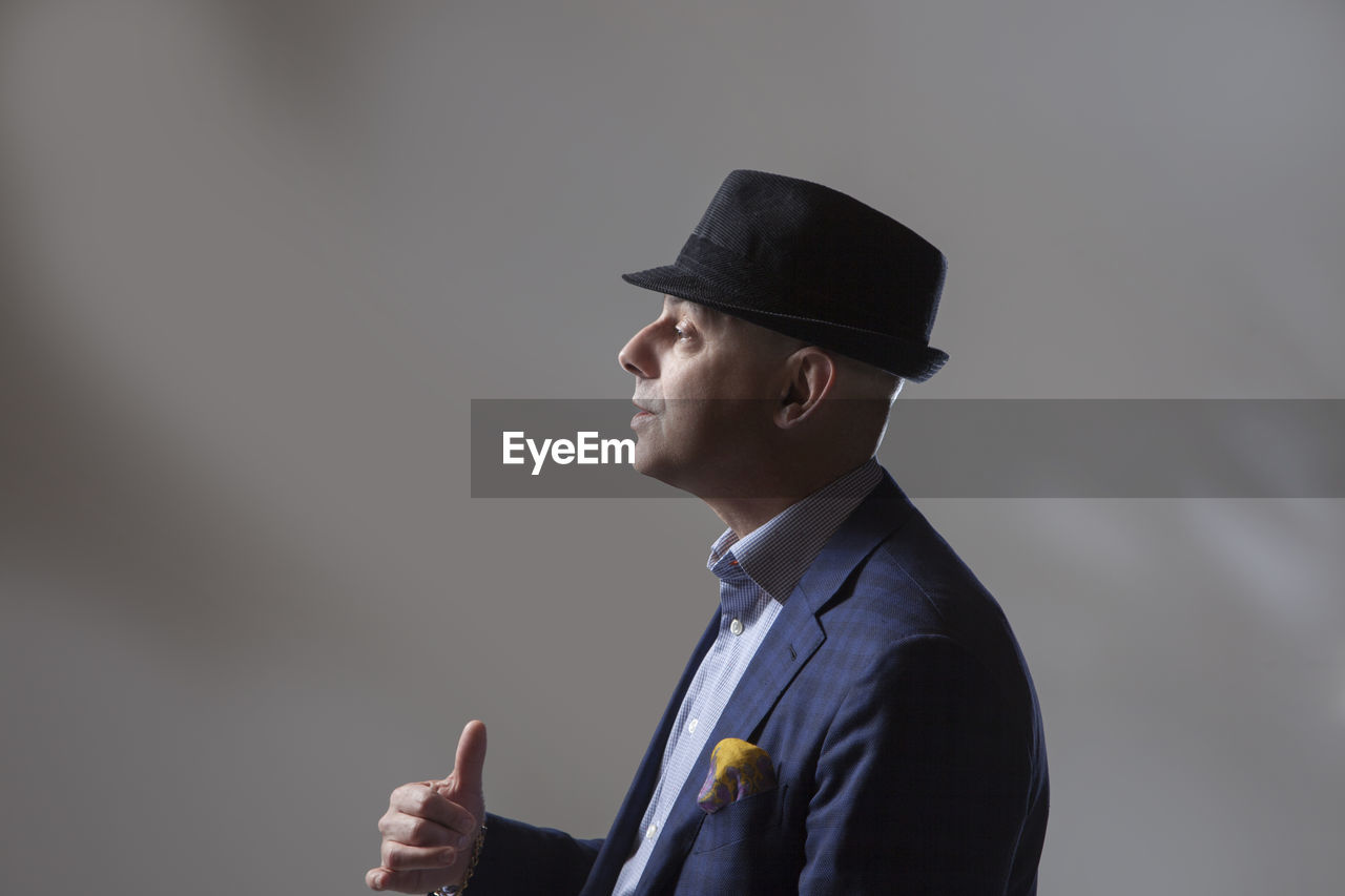 Side view of mature businessman showing thumbs up against gray background