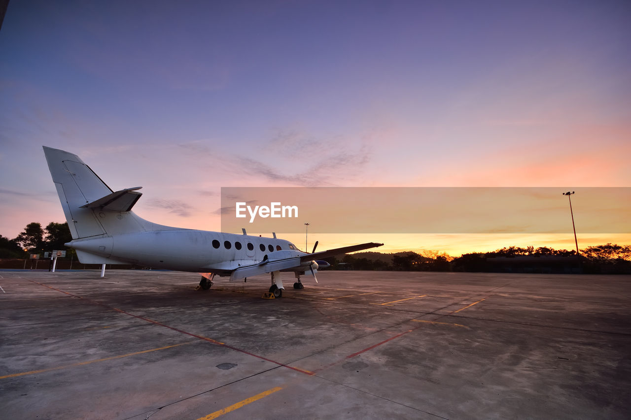 AIRPLANE ON RUNWAY AGAINST SKY AT SUNSET