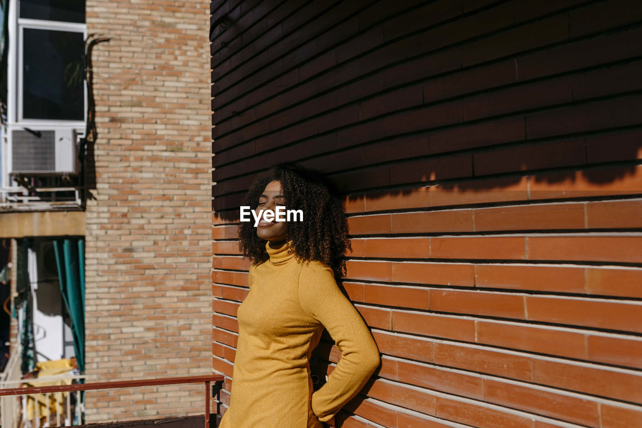 Smiling woman with hands behind back leaning on wall