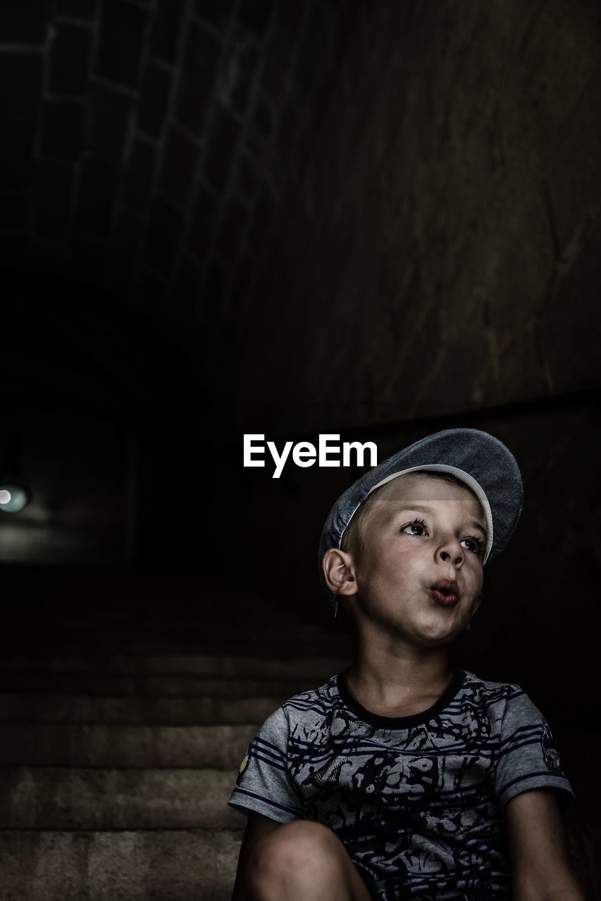 Thoughtful boy wearing cap while sitting on steps in tunnel