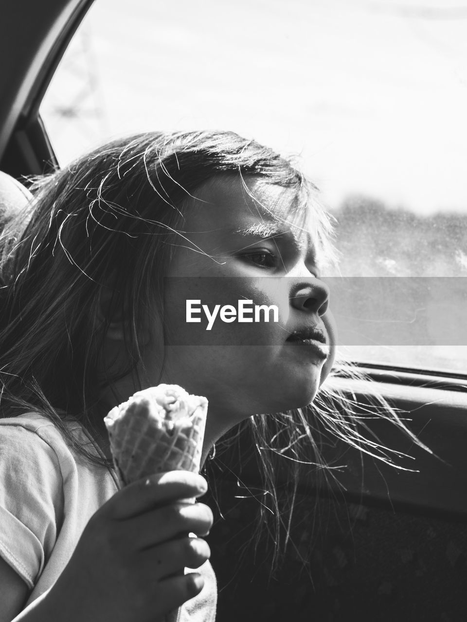 Girl holding ice cream cone while looking away in car