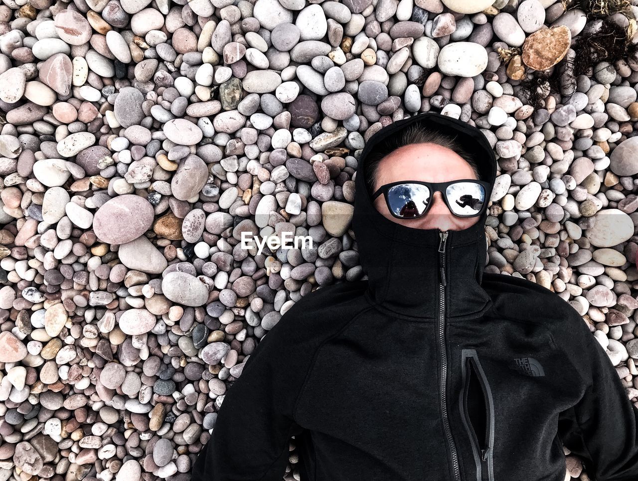 Directly above shot of man wearing sunglasses while lying on pebbles