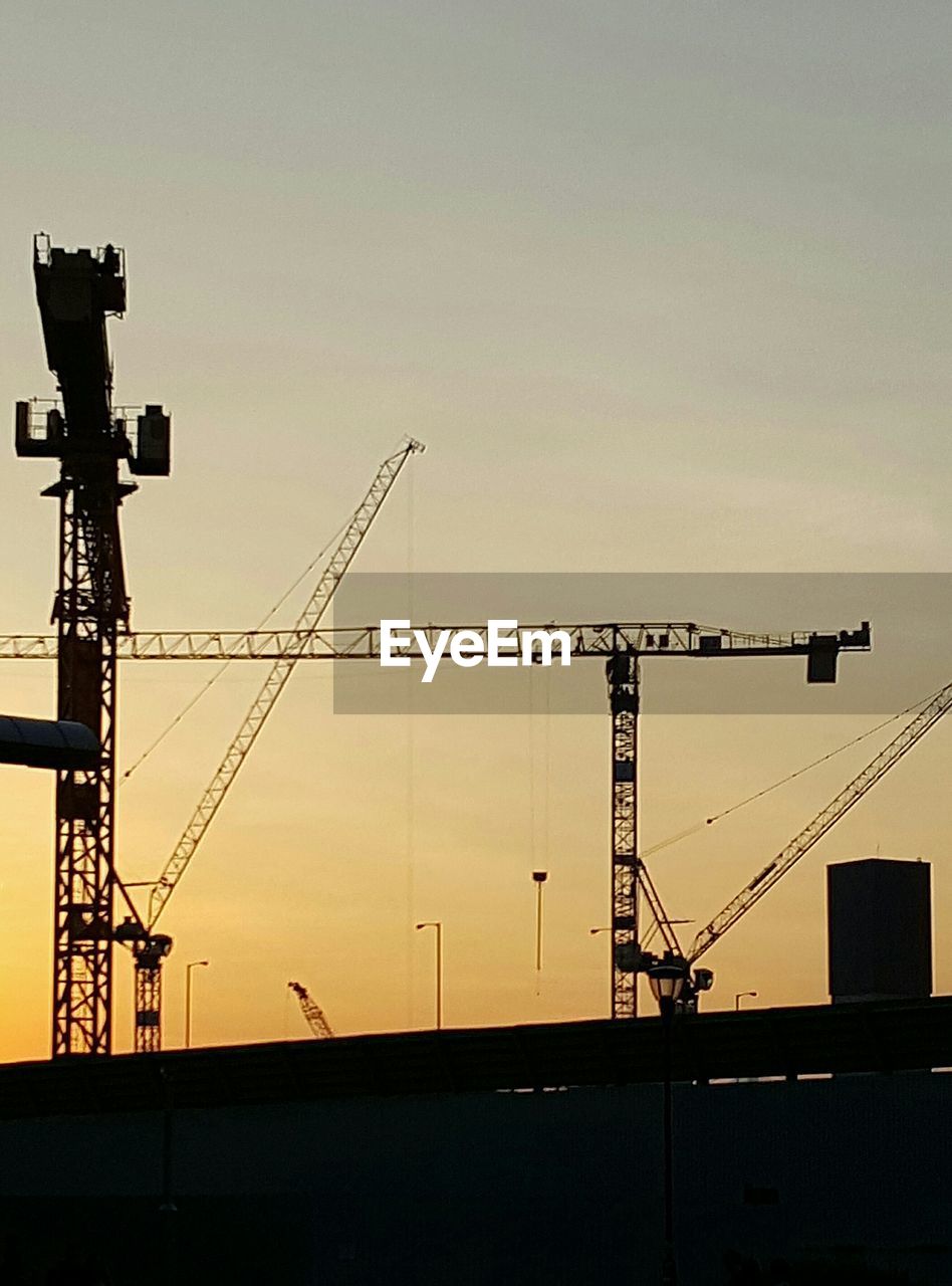 LOW ANGLE VIEW OF CRANES AT CONSTRUCTION SITE