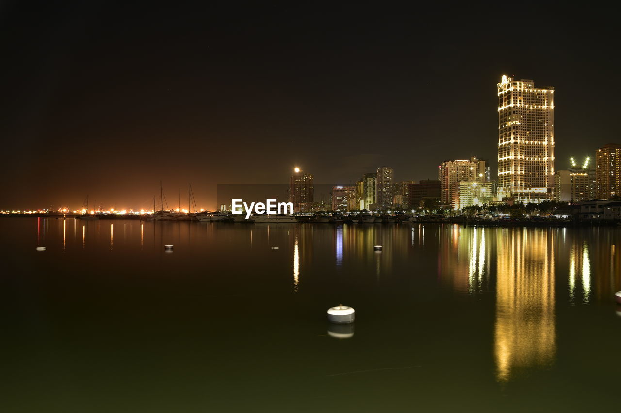 Illuminated cityscape by sea against sky at night