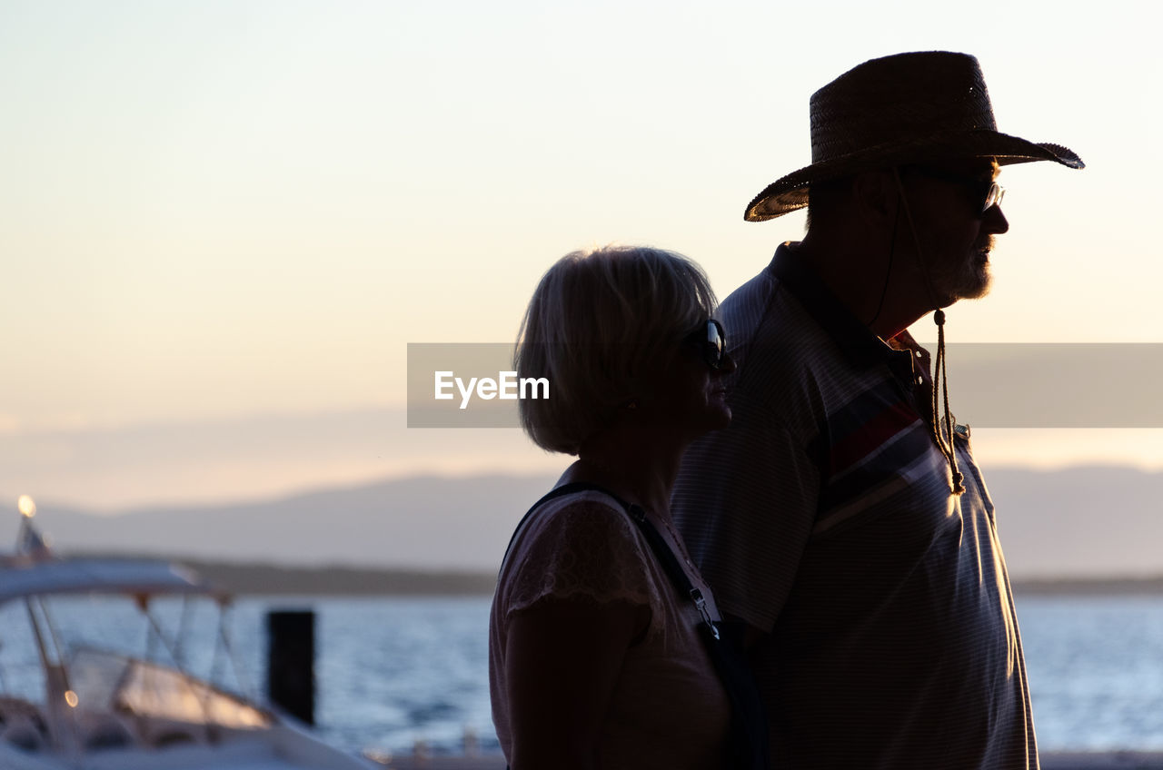 REAR VIEW OF MAN AND WOMAN LOOKING AT SEA AGAINST SKY