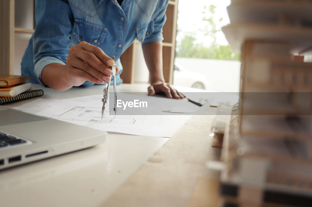 Midsection of female architect using drawing compass on blueprint at desk