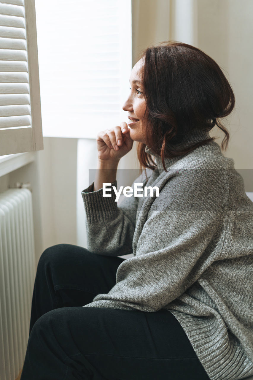 Young woman looking away while sitting on sofa at home