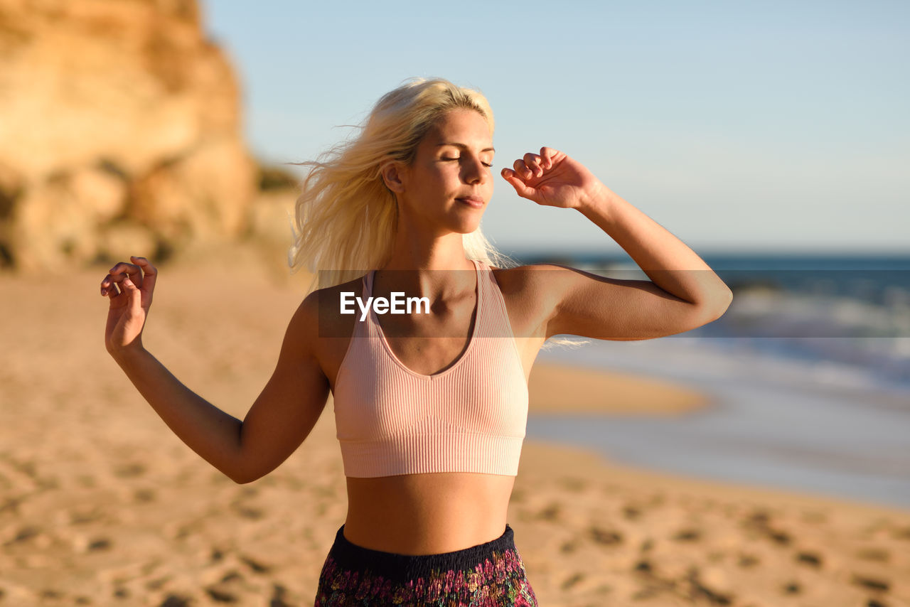 Woman with closed eyes standing at beach against clear sky
