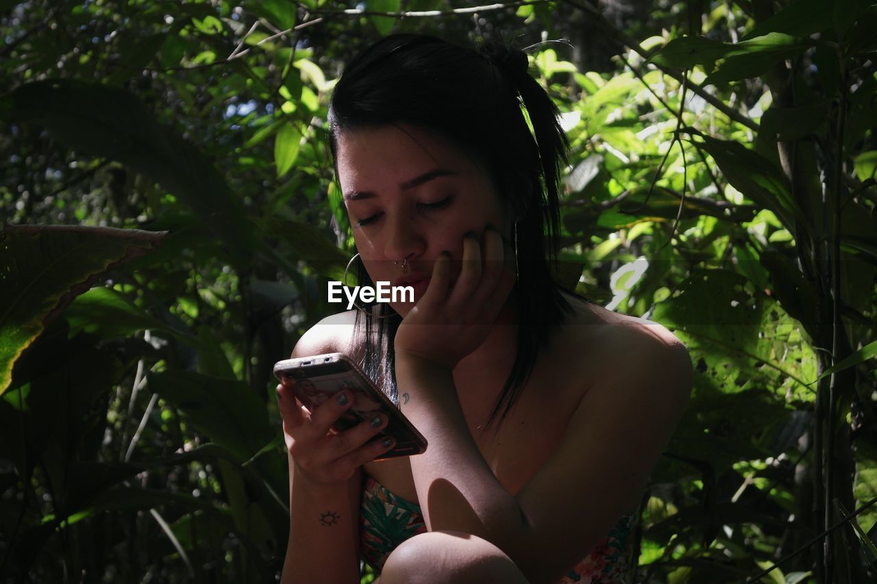 Close-up of young woman using mobile phone against trees