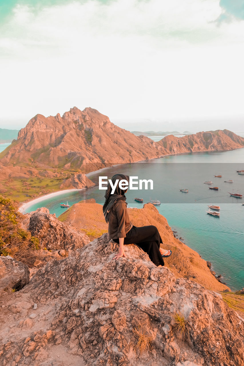 REAR VIEW OF MAN LOOKING AT ROCK FORMATION IN WATER