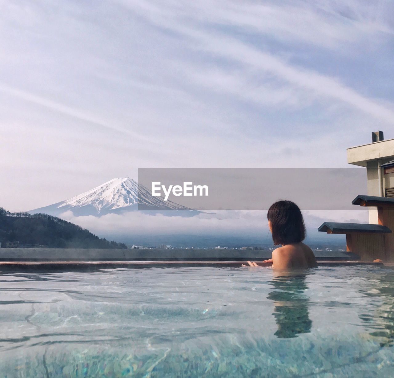 Rear view of shirtless woman in hot spring against snowcapped mt fuji