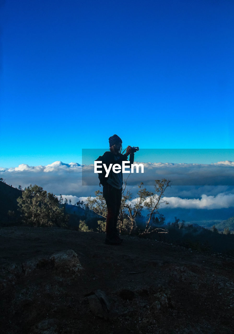 Woman photographing while standing on land against sky