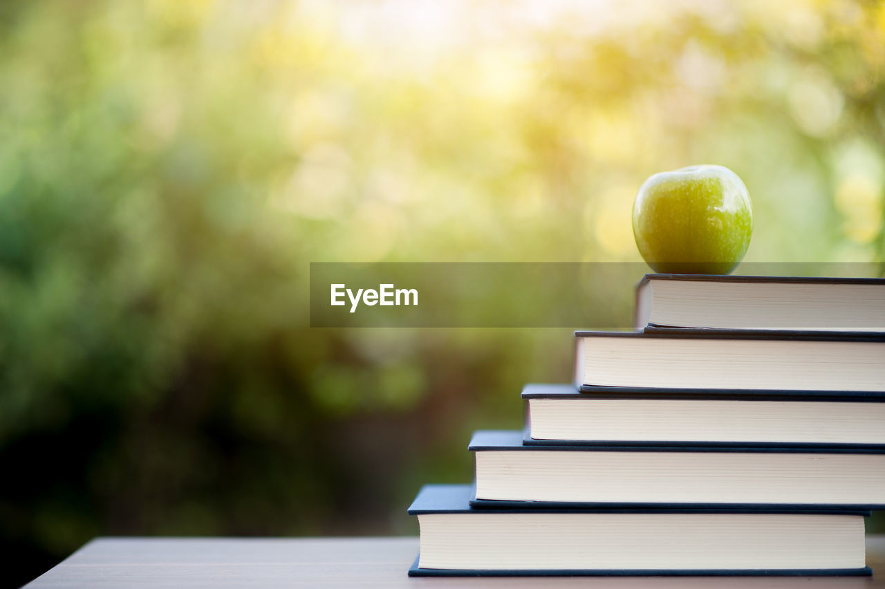 CLOSE-UP OF APPLE ON WOODEN TABLE AND STACK OF BOOKS ON WOOD