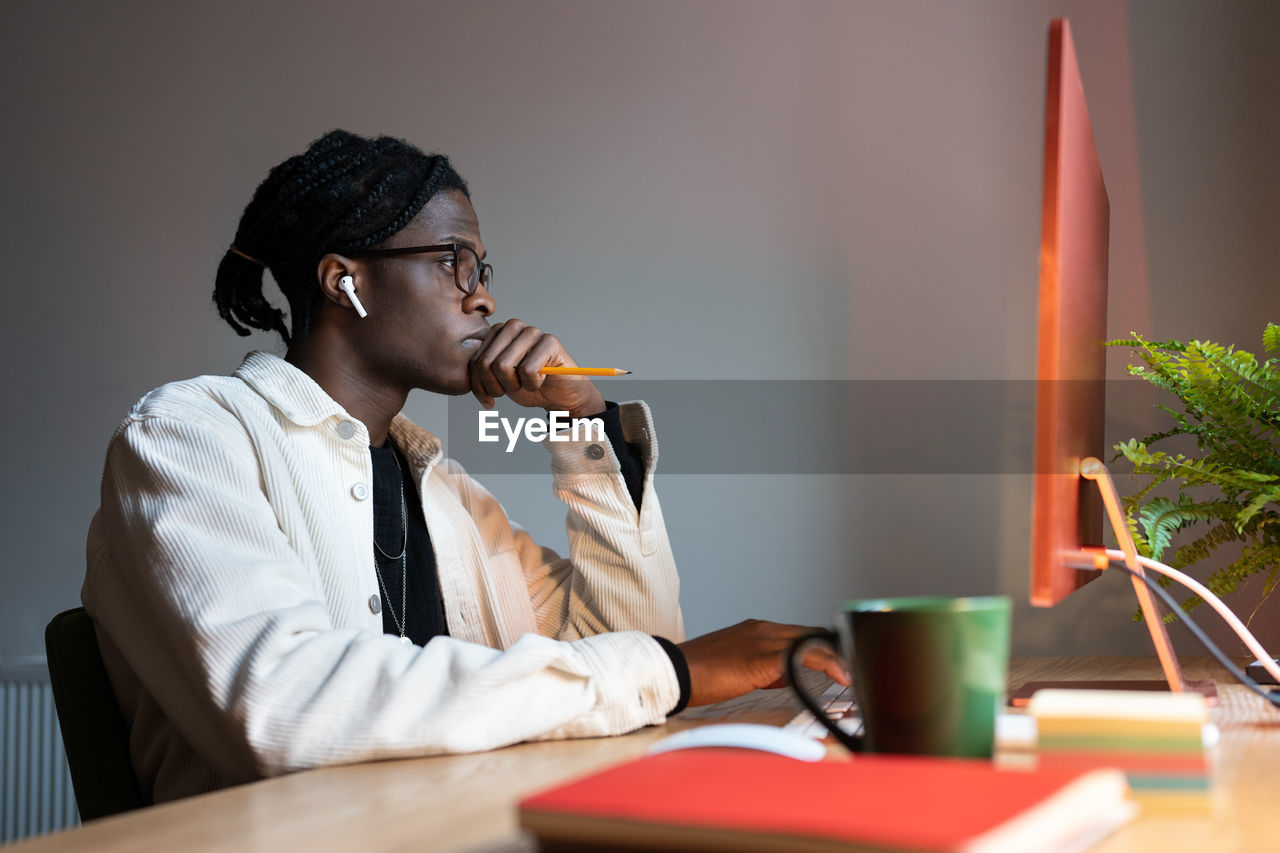 young man using mobile phone while sitting on table in office