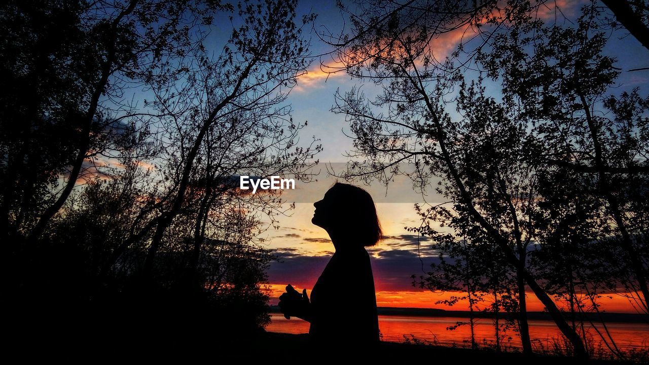 Silhouette woman standing by trees during sunset
