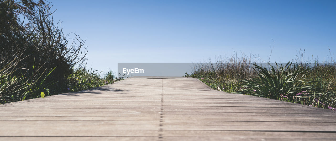 Close up view of wooden walkway leading to the sea through low mediterranean vegetation path of wood