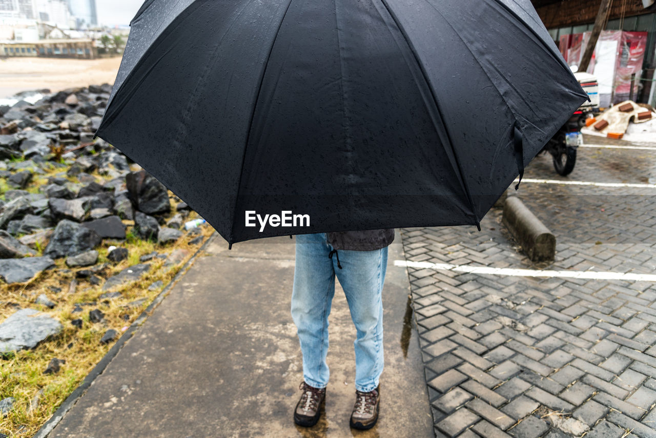 Low section of woman with umbrella walking on street