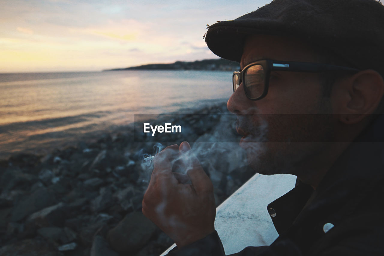Side view of man smoking cigarette at beach during sunset