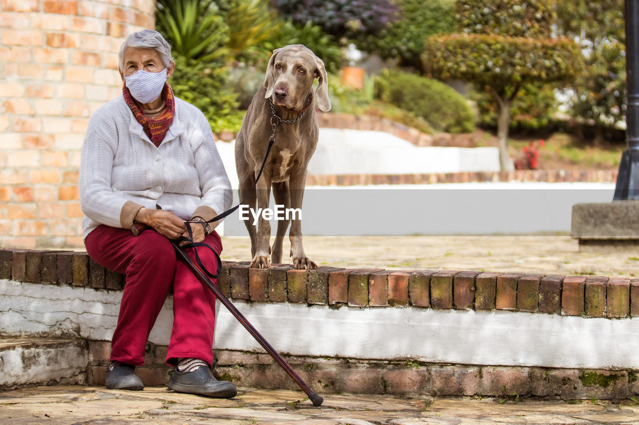 FULL LENGTH PORTRAIT OF MAN HOLDING DOG WHILE SITTING ON STREET