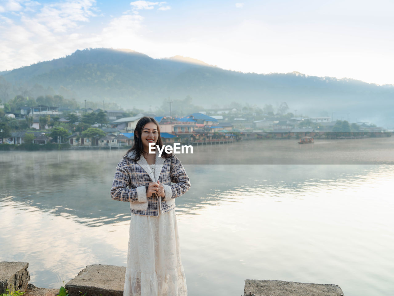 Happy asian woman standing at lakeside with fog on the lake view in morning at ban rak thai village