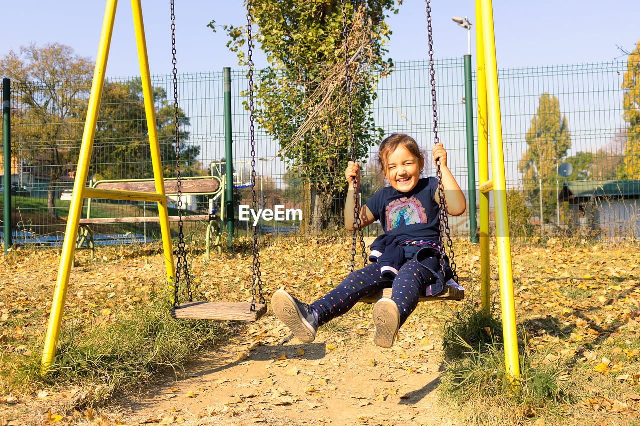 Full length of smiling girl on swing at park