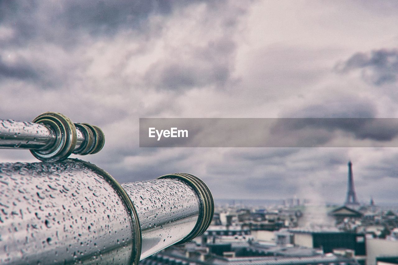 Close-up of cityscape against cloudy sky with telescope