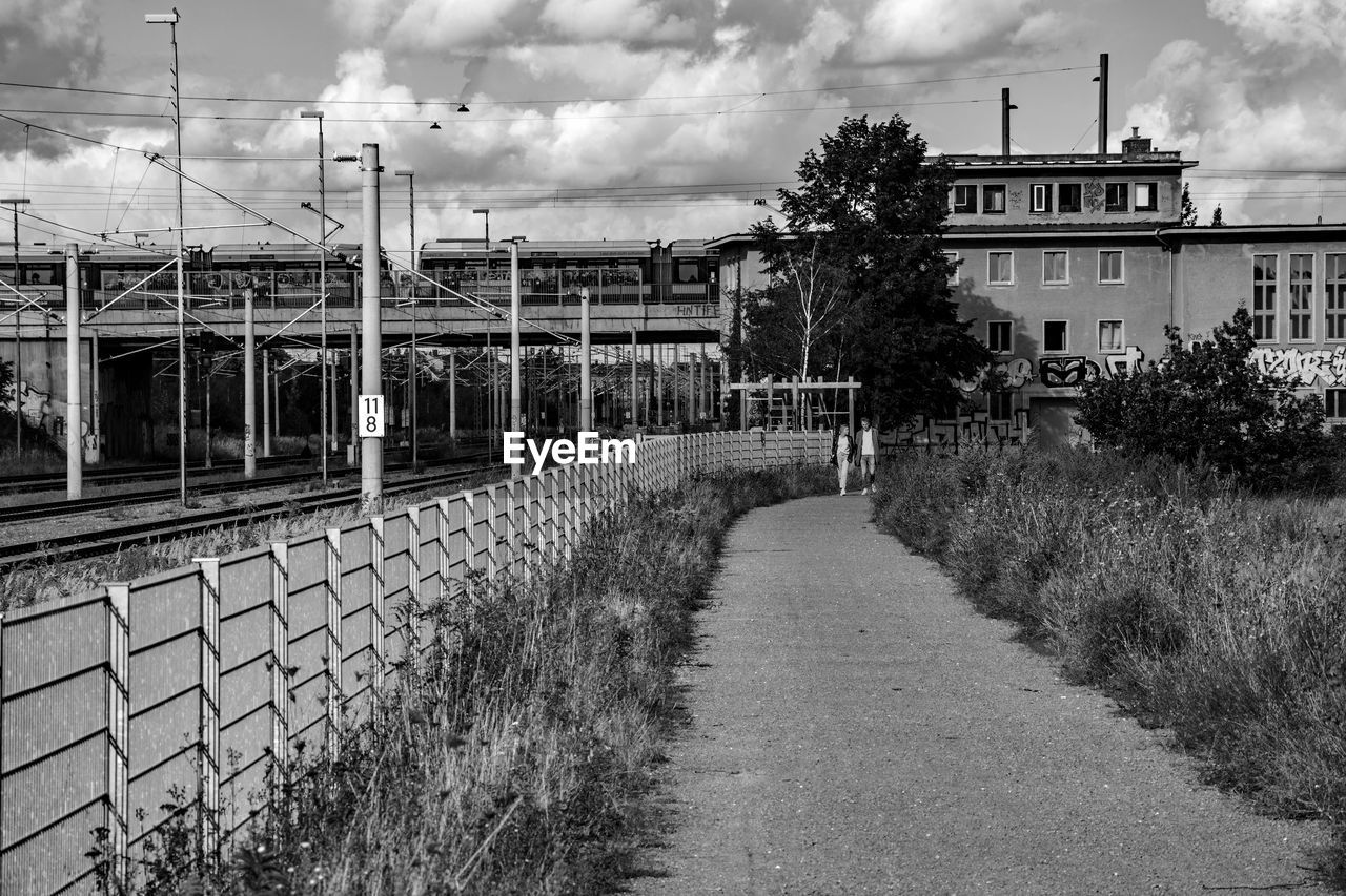 cloud, architecture, transport, sky, built structure, urban area, building exterior, nature, plant, black and white, monochrome, road, monochrome photography, transportation, no people, day, city, waterway, outdoors, street, tree, building, residential area, track, railway, fence, the way forward