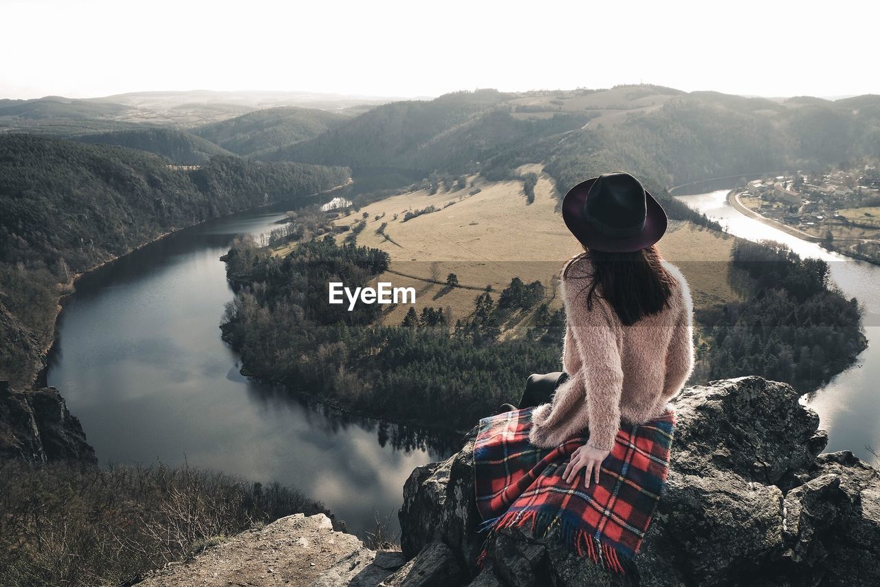 Rear view of woman sitting on cliff against river