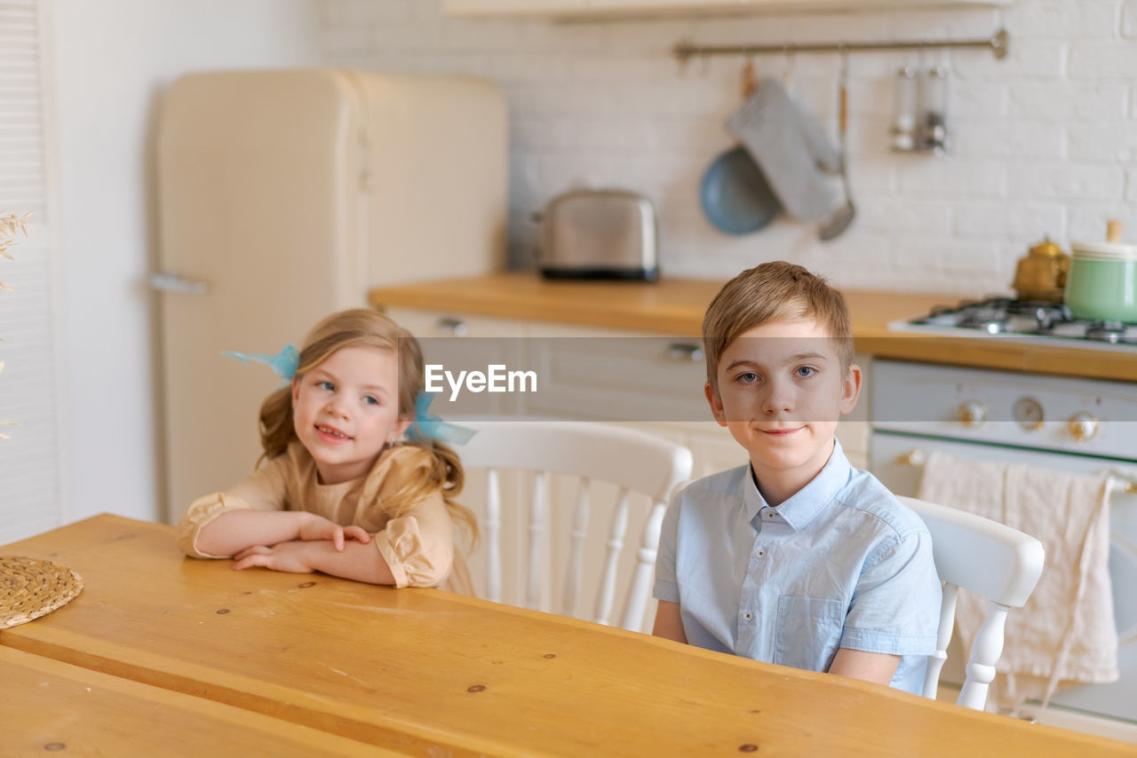 Children sit at table in kitchen and wait for their parents to make them