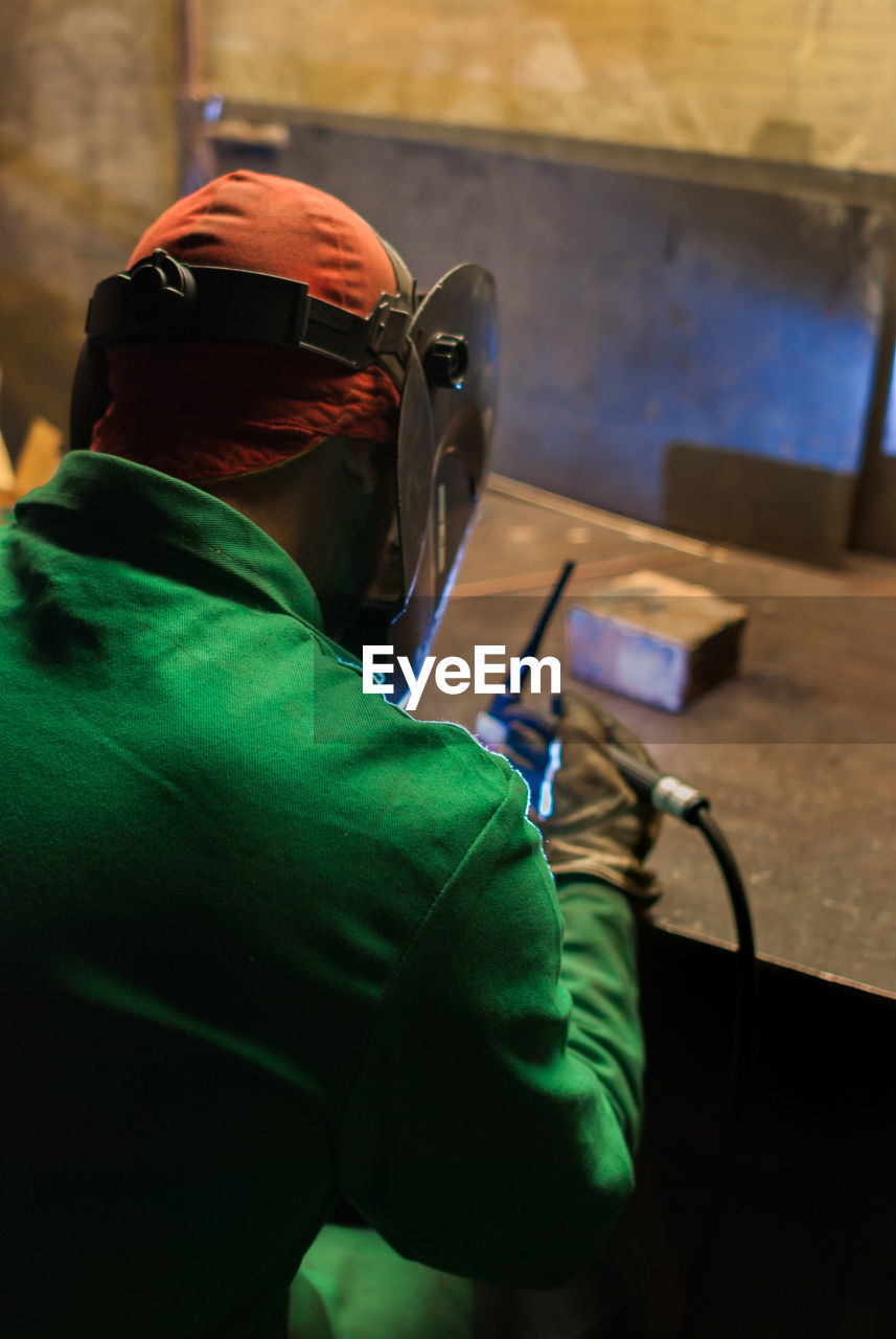 REAR VIEW OF MAN WORKING IN ILLUMINATED MIRROR