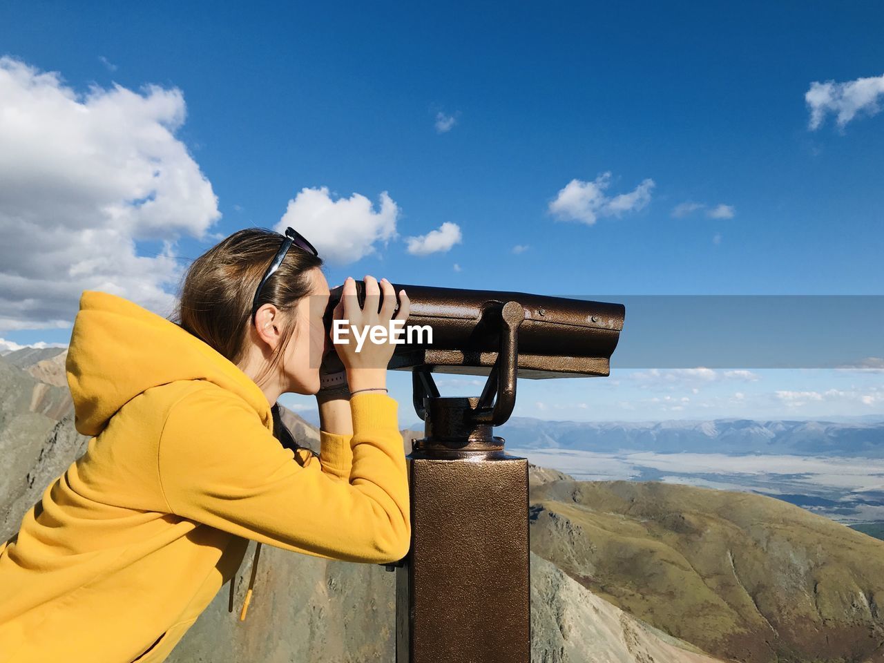 Side view of woman looking though binoculars against sky