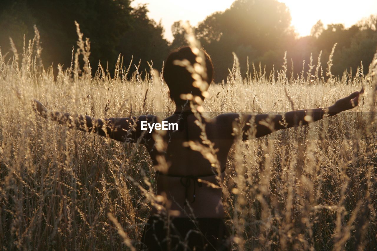 Rear view of young woman with arms outstretched standing on field
