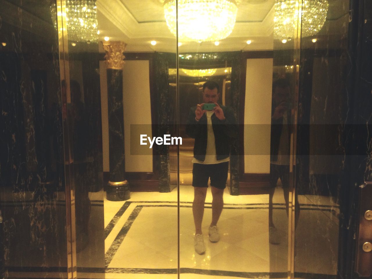 Reflection of man clicking photograph on elevator door