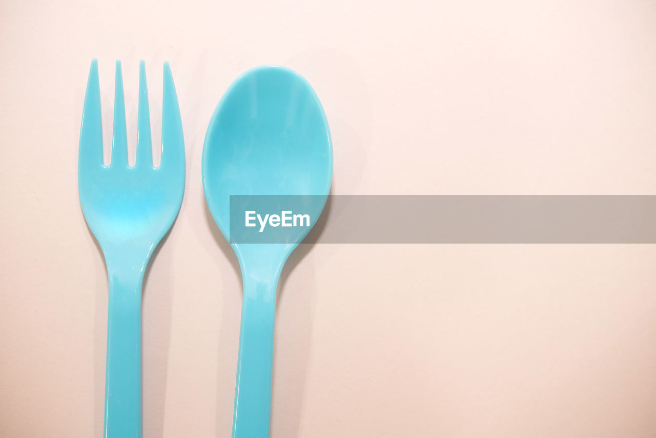 Close-up of disposable plastic fork and spoon on colored background