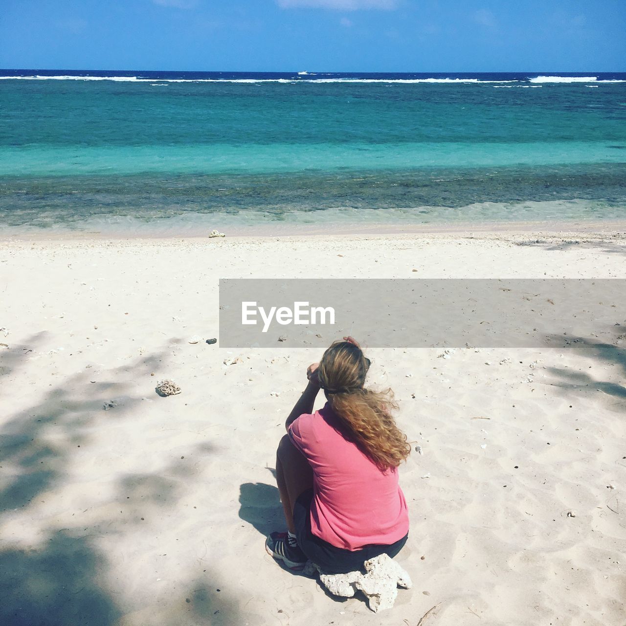 REAR VIEW OF WOMAN SITTING ON SHORE AT BEACH