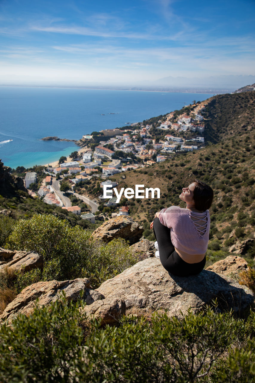 Woman sitting on rock against townscape and sea