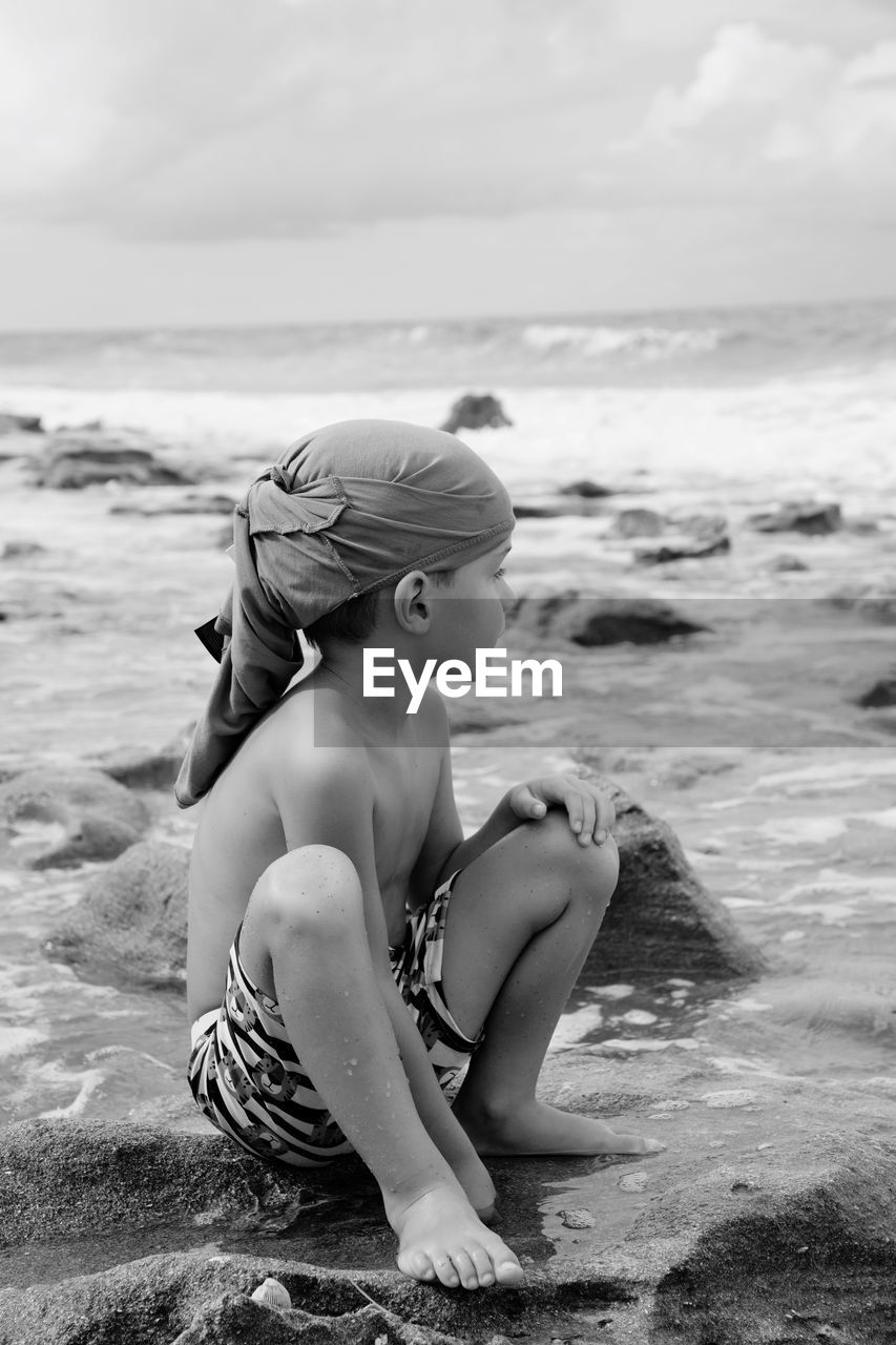 Child sitting on rock at beach against sky