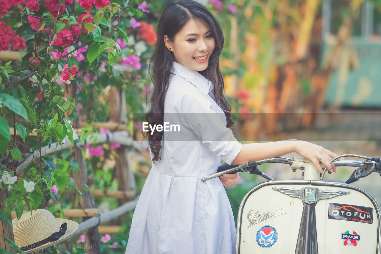 Side view of smiling young woman standing by motor scooter