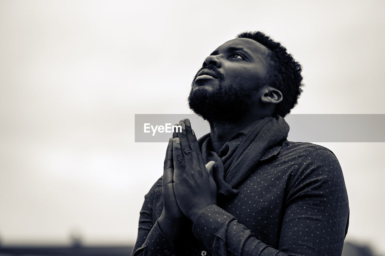 Close-up of man with hands clasped against sky