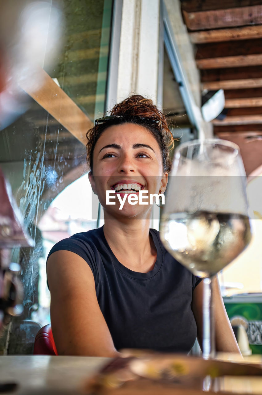 Smiling young woman with a glass of white wine on the table