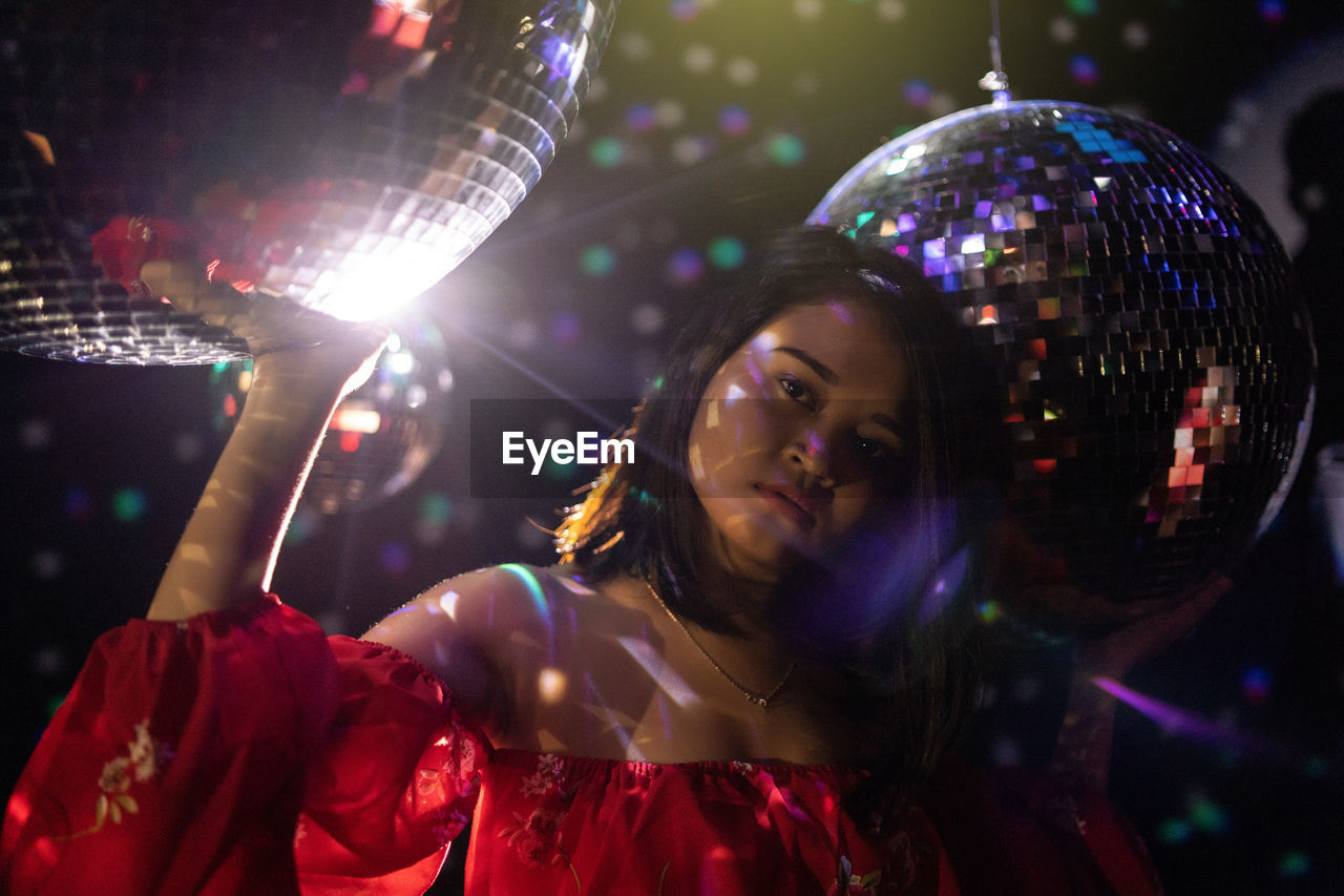 Portrait of young woman standing amid disco balls at nightclub
