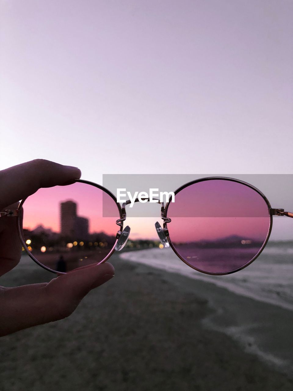 Cropped hand holding sunglasses against clear sky during sunset