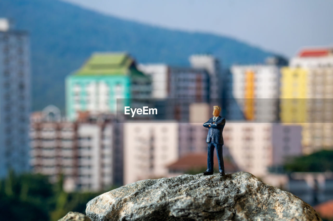 MAN STANDING ON ROCK IN CITY AGAINST BUILDINGS