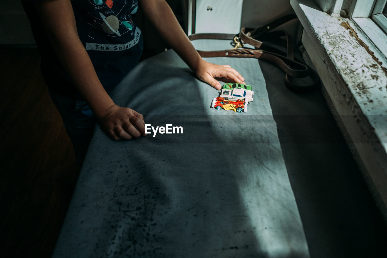 Young child lining up toy cars in a pocket of sunlight near window