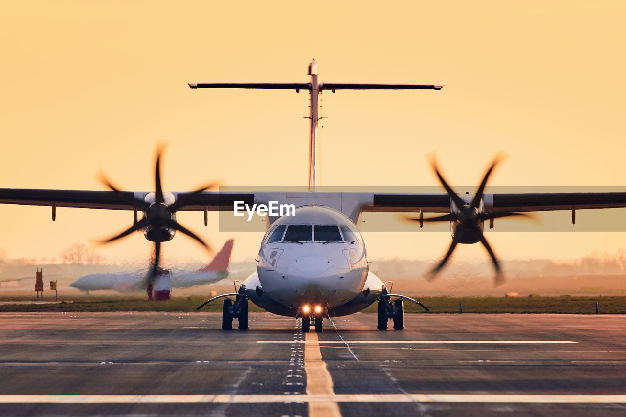 Airplane on runway against sky during sunset