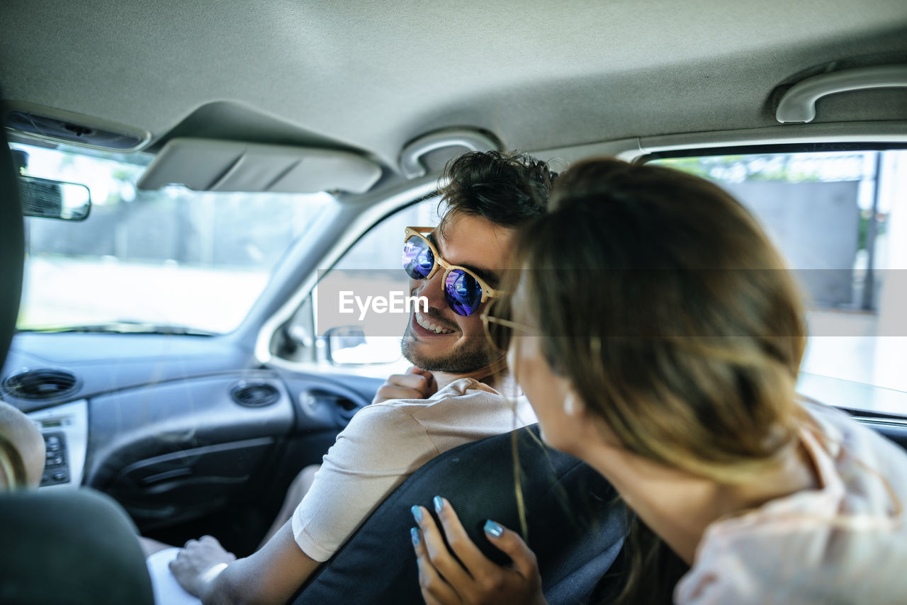 Man in passenger seat of a car talking to a woman from the backseat