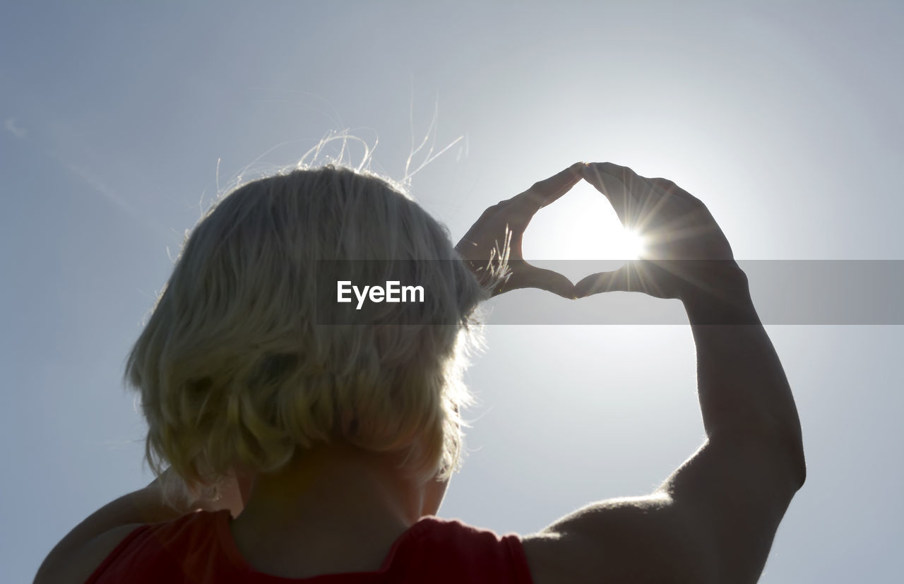 Rear view of woman making heart shape with hands against sky