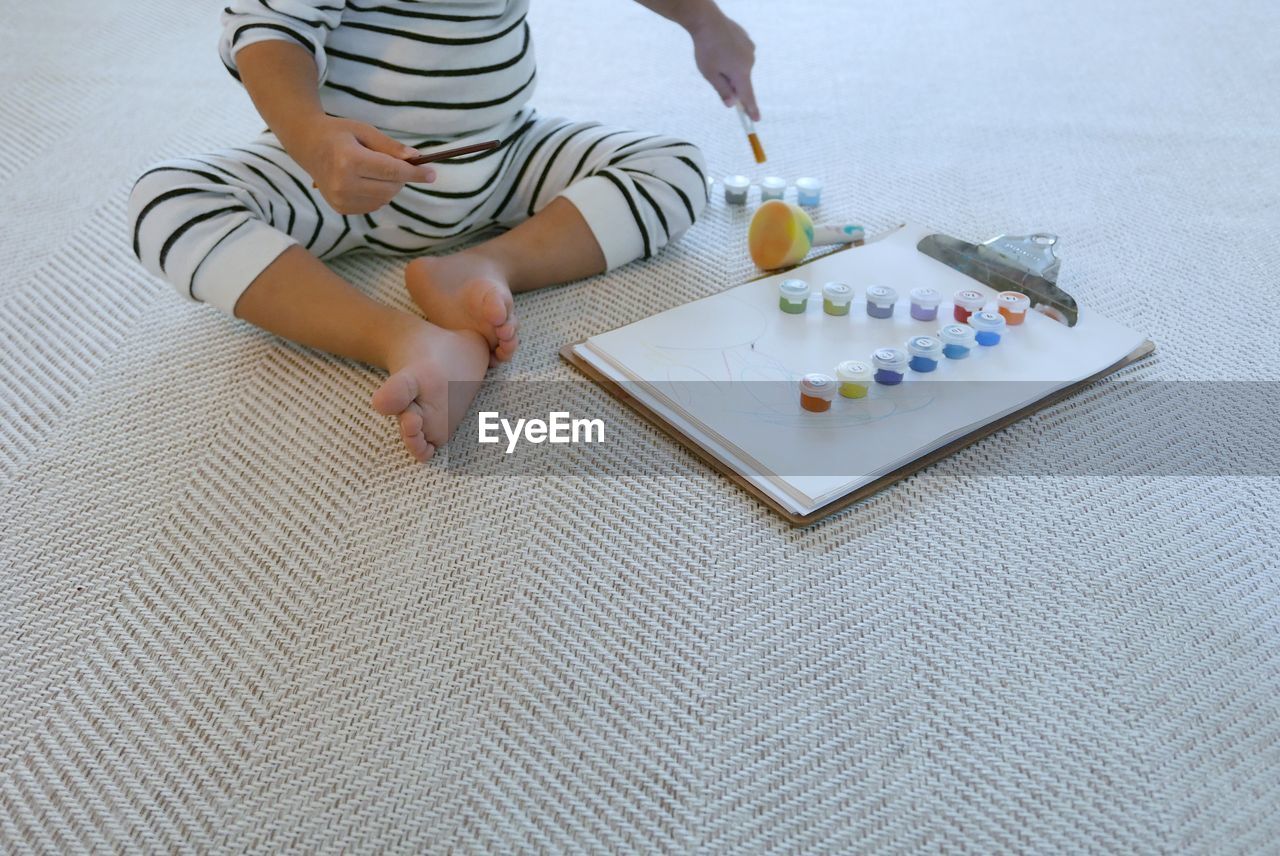 Low section of boy with watercolor paints sitting on carpet at home